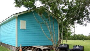 A small blue shed with a picnic table and two barbecue grills in front.