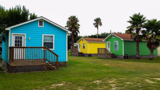 A row of colorful houses with a grassy yard and palm trees.