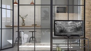 Een moderne woonkamer met een grote flatscreen televisie op een glazen plank, een salontafel en twee barkrukken.