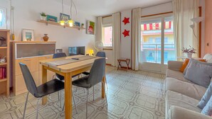 A modern living room with a dining area, featuring a large window with curtains, a sofa, a dining table with chairs, and a small side table.