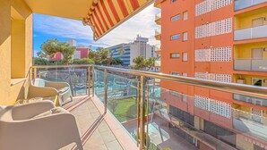 A balcony with a glass railing, a striped awning, and a view of a parking area and buildings in the background.