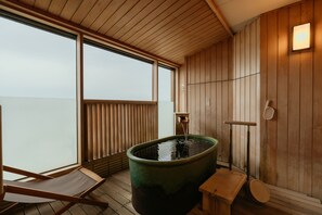A wooden spa room with a large hot tub, a wooden bench, and a window with blinds.