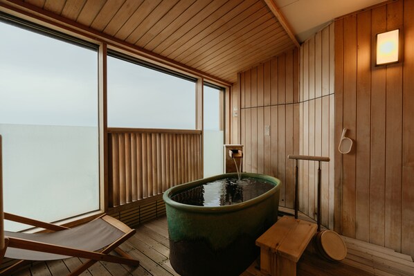 A wooden spa room with a large hot tub, a wooden bench, and a window with blinds.
