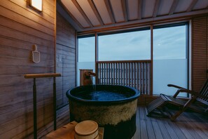 A wooden deck with a hot tub, a wooden chair, and a view of the sea.