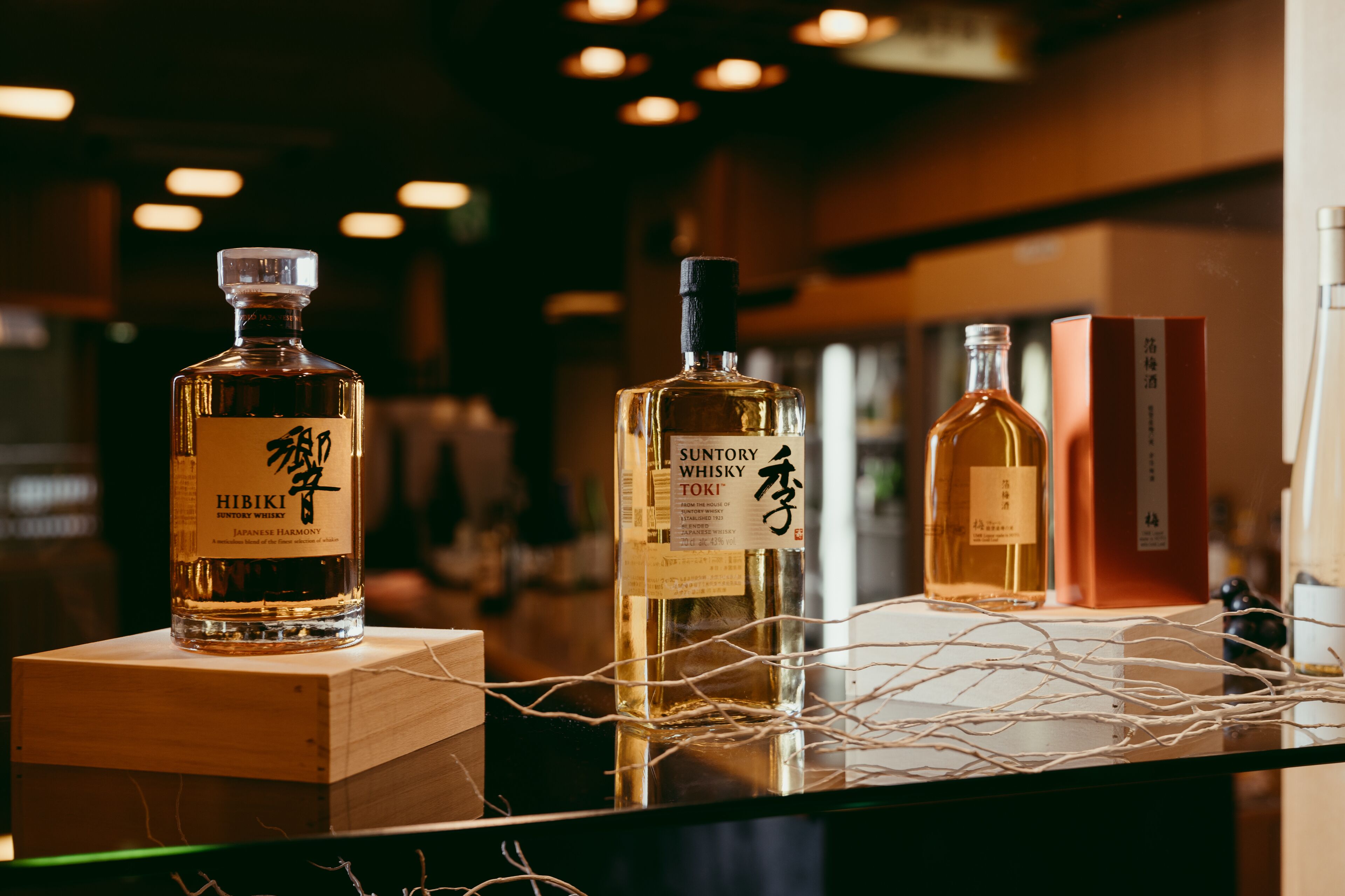 Tres botellas de whisky japonés exhibidas junto con cajas de madera y un adorno de cuerda.