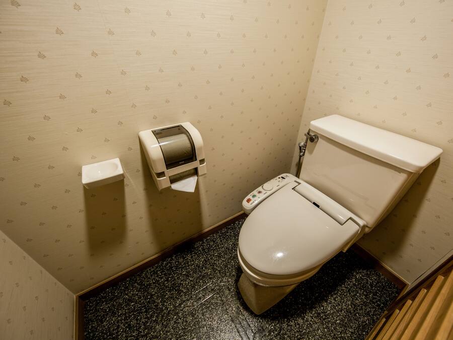 A small bathroom with a toilet, a paper towel dispenser, and a toilet paper roll on the wall.