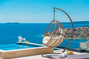 Un fauteuil suspendu au bord d’une piscine, avec vue sur la mer et le paysage urbain.
