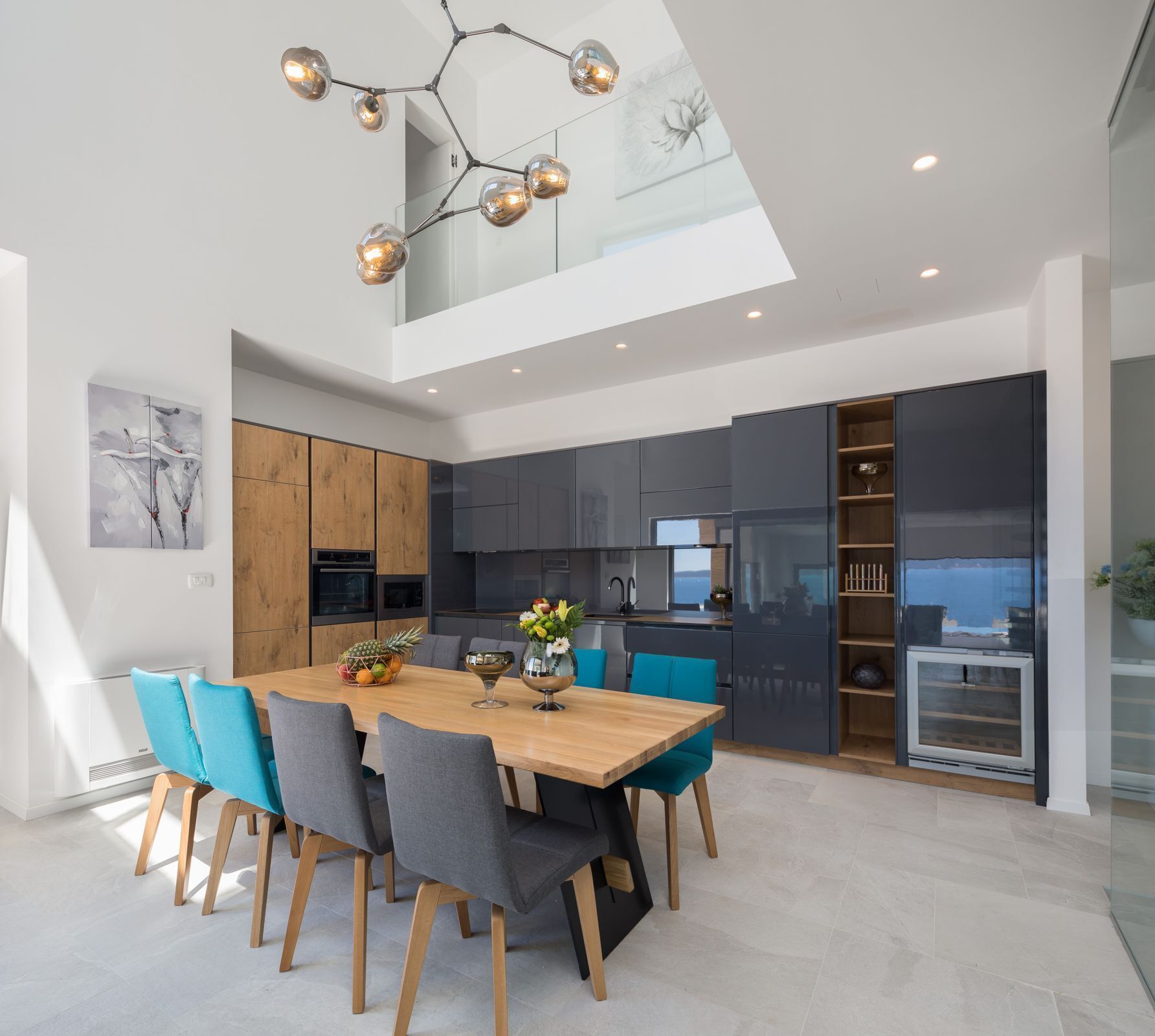 Een moderne keuken met donkere kastjes, een houten eettafel en turquoise stoelen.