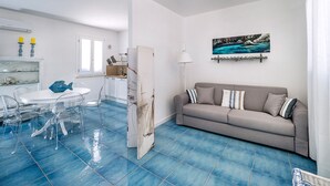A modern living room with a grey sofa, a dining table with chairs, and a kitchen area with white cabinets. - House with terrace, 80 metres from beach of San Vito lo Capo, Sicily (San Vito Lo Capo)