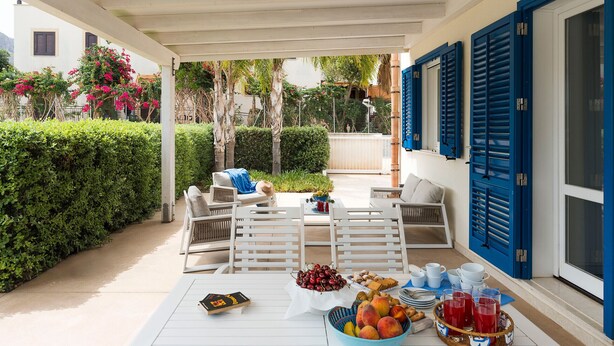 A covered outdoor dining area with white furniture, a table set with fruits, drinks, and a book. - House with terrace, 80 metres from beach of San Vito lo Capo, Sicily (San Vito Lo Capo)