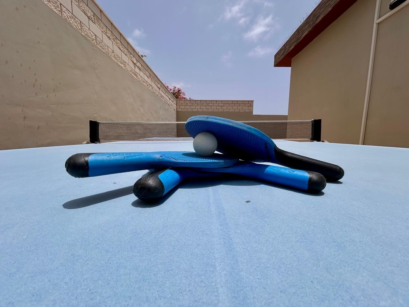 A ping pong table with a blue tablecloth, a blue paddle, and a white ball.