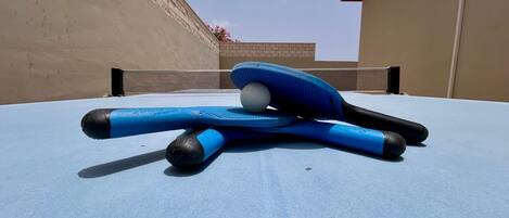 A ping pong table with a blue tablecloth, a blue paddle, and a white ball.