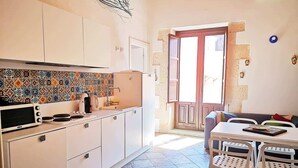Cocina compacta con gabinetes blancos, microondas y estufa. Zona de comedor con mesa y sillas.