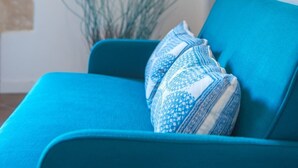 Un sofá color turquesa con un cojín estampado en una sala de estar moderna con una pared blanca y decoración en la pared.