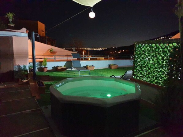 Relax in a serene outdoor oasis with a hot tub, lounge chairs, and lush greenery.