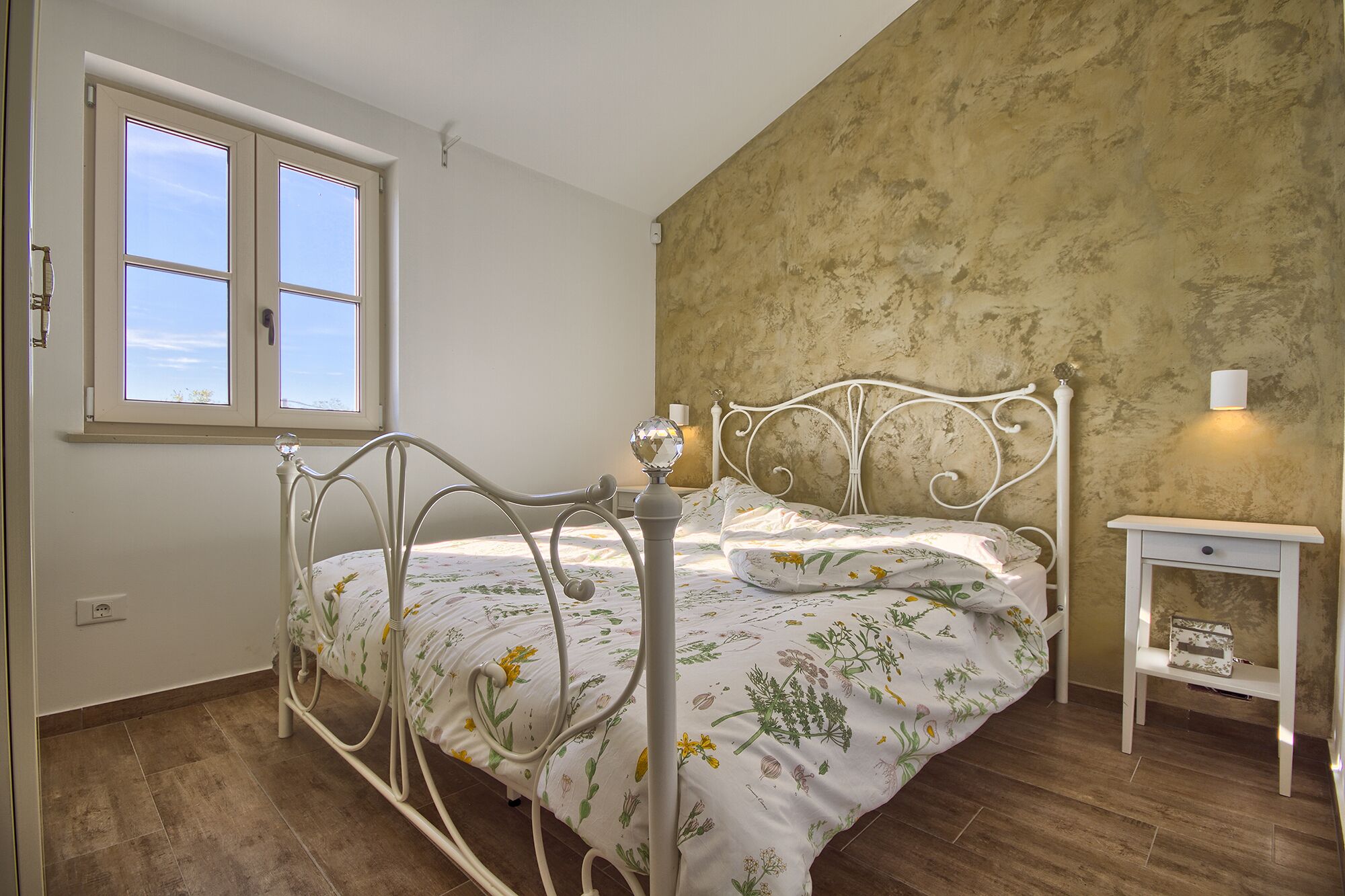 A bedroom with a bed, a nightstand, a window, and a wall with a textured finish.