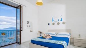 A bedroom with a bed, a nightstand, a dresser, a window with a view of the sea, and a wall with nautical decorations.