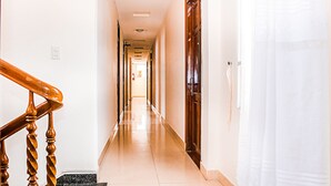A hotel hallway with a wooden staircase on the left, a door on the right, and a light-colored floor.