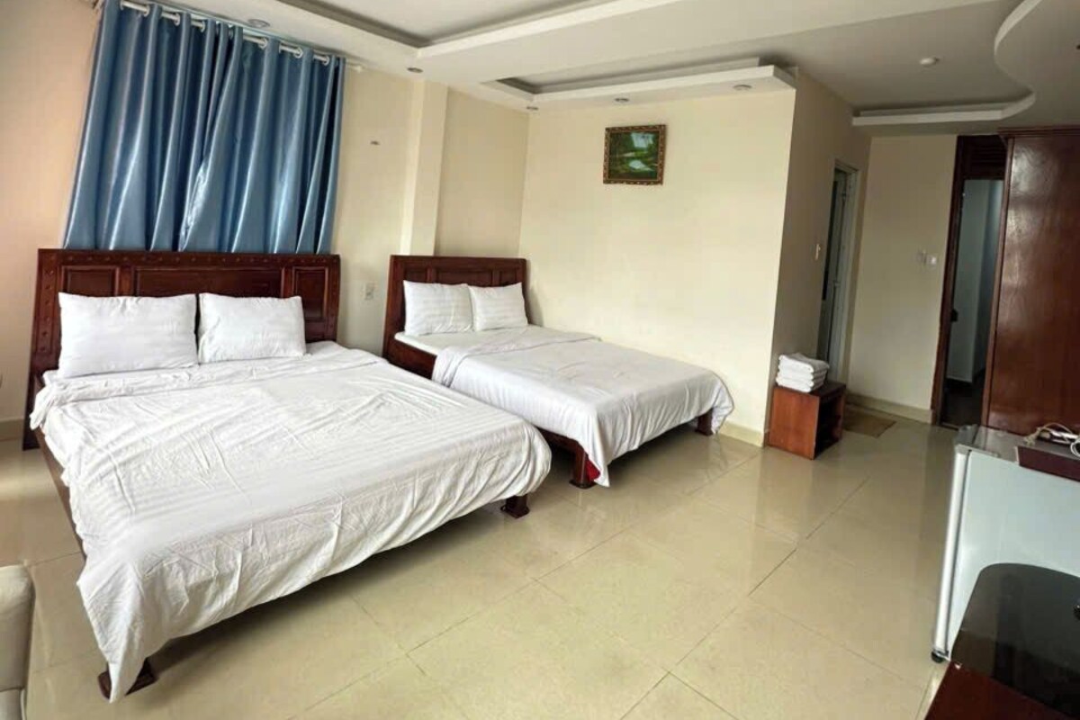 A hotel room with two beds, a wooden headboard, a small table, and a ceiling design.