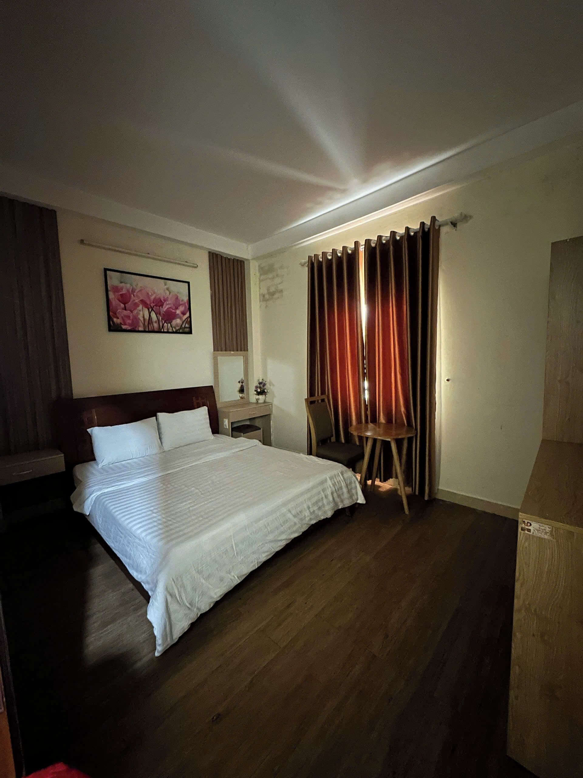 A hotel room with a large bed, a desk, a chair, and a painting on the wall.