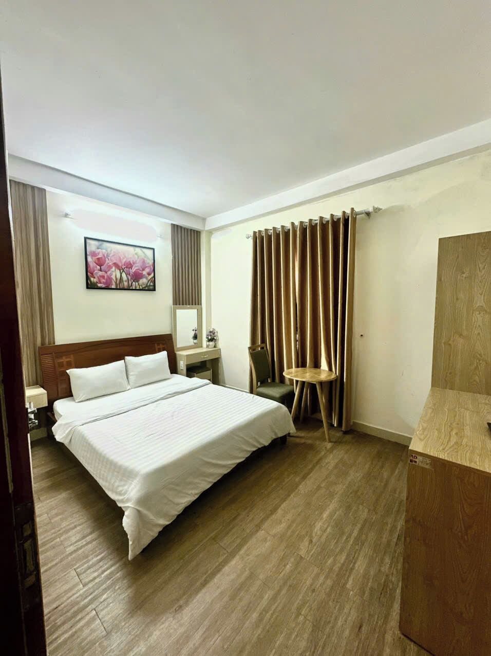 A hotel room with a large bed, a bedside table, a chair, a small round table, and a mirror.