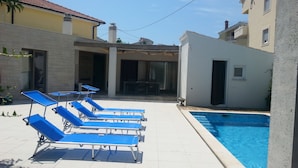 Un área de piscina con sillones reclinables azules y una pequeña mesa.