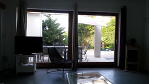 Un salón con televisión, una mesa de vidrio y una silla. Hay una puerta corrediza de vidrio que da a un patio exterior con una mesa y sillas.