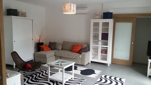 Una sala de estar con sofá, una mesa de centro de vidrio, una silla, un armario y un televisor.