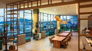 A modern hotel lobby with a long dining table, comfortable seating, and large windows offering a city view. - DARAKHYU Yeosu Capsule Hotel by WALKERHILL (Yeosu)