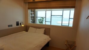 A bedroom with a bed, a window with a view of the sea, a bedside table, and a small plant. - DARAKHYU Yeosu Capsule Hotel by WALKERHILL (Yeosu)