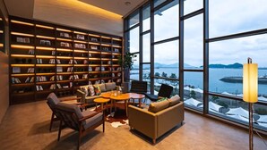 A modern library with large windows overlooking a body of water and mountains. - DARAKHYU Yeosu Capsule Hotel by WALKERHILL (Yeosu)