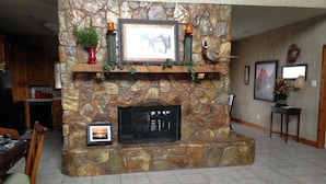 A stone fireplace with a mantel, surrounded by a dining area with chairs and a table. - Beautiful Lakefront Home-Lake Alan Henry (Justiceburg)