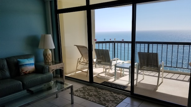 A living room with a sofa, a coffee table, and a view of the ocean through large windows. - Direct Oceanfront Condo, Amazing Views of Ocean and Bay (Ocean City)