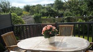 A wooden deck with a round table and four chairs, surrounded by a wooden fence and lush greenery. - nice quiet house  (Quimper)