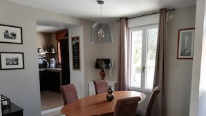 A dining area with a wooden table and chairs, a pendant light, and a view of the kitchen and outside through a window. - nice quiet house  (Quimper)