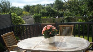A wooden deck with a round table and four chairs, surrounded by a wooden fence and lush greenery.