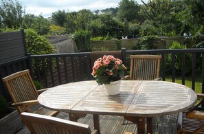Une terrasse en bois avec une table ronde et quatre chaises, entourée d’une clôture en bois et d’une végétation luxuriante.