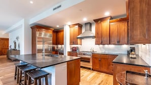 Una cocina moderna con armarios de madera, una estufa de acero inoxidable y una isla central con taburetes.