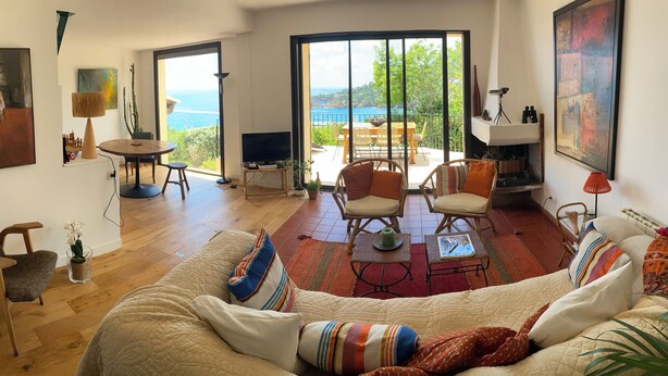 Un salón amplio con un sofá grande, una zona de comedor con mesa y sillas, un televisor y un balcón con vistas al mar.