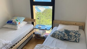 Un dormitorio con dos camas, una ventana con vistas al mar y barcos, y suelo de madera.