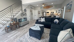 Ein modernes Wohnzimmer mit Treppe, einem dunkelgrauen Sofa und einer Küche im Hintergrund.