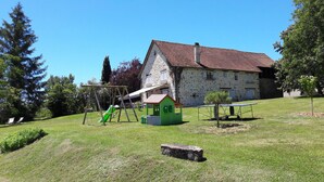 Een stenen huis met een rode pannendak, een klein groen poppenhuis en een schommel.