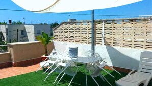 Une terrasse extérieure avec du gazon synthétique, des chaises en plastique blanches et une table.