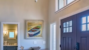 Un hall spacieux agrémenté d’un grand lustre, d’un tableau représentant un bateau, d’une porte en bois sombre et d’une petite table décorée d’une étoile de mer.