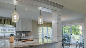 Une cuisine moderne dotée d’un grand îlot central, de luminaires suspendus et donnant sur un patio extérieur.