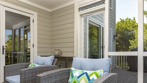 Une terrasse couverte, aménagée avec des meubles en osier et dotée d’une porte vitrée donnant sur un espace extérieur.