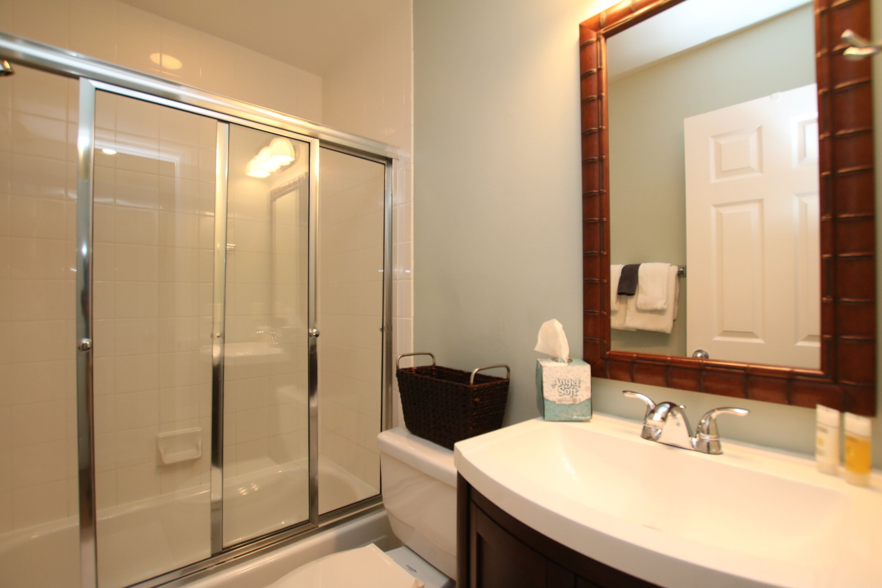 A bathroom with a glass shower enclosure, a white sink, and a mirror with a wooden frame.