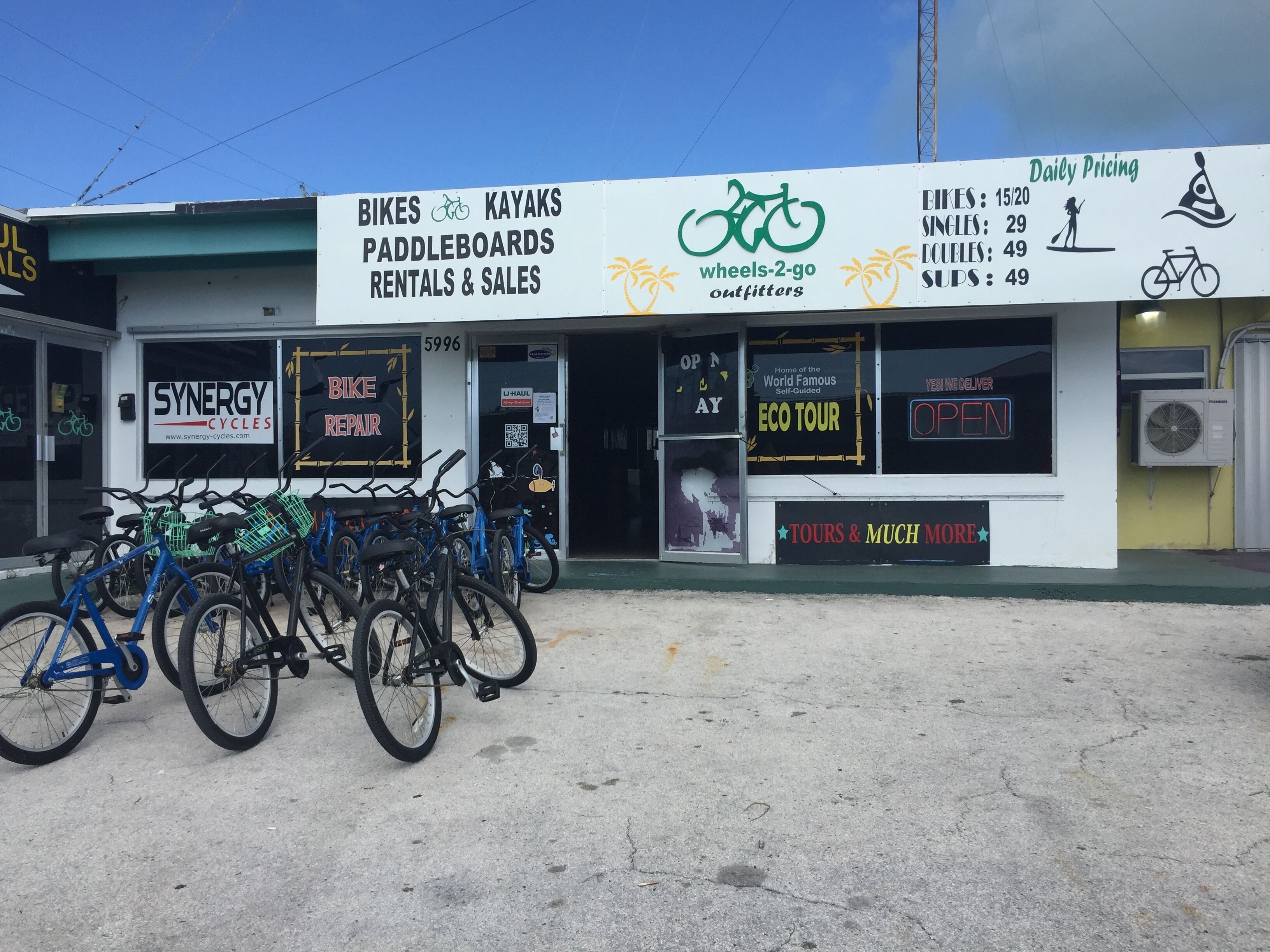 Fachada de loja com placas indicando aluguel de bicicletas, venda de caiaques e aluguel de pranchas de paddleboard.