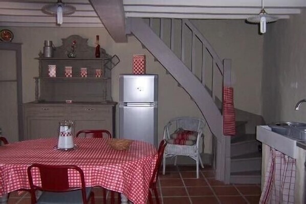 A kitchen with a dining table, chairs, a refrigerator, and a staircase.