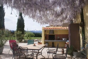 An outdoor patio with a table and chairs, a barbecue grill, and a view of mountains in the background.